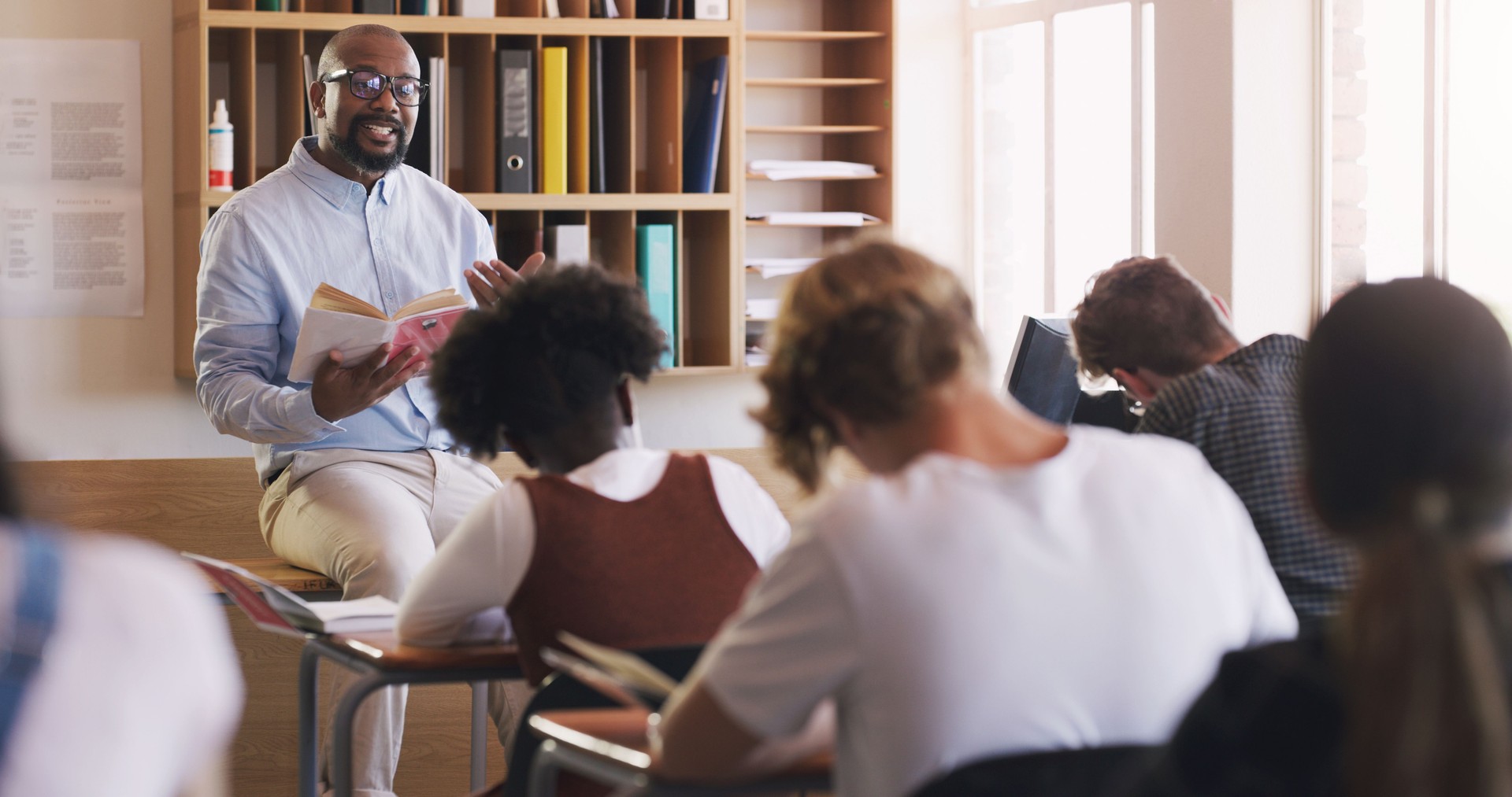 Shot of man reading a book to his students in a classroom